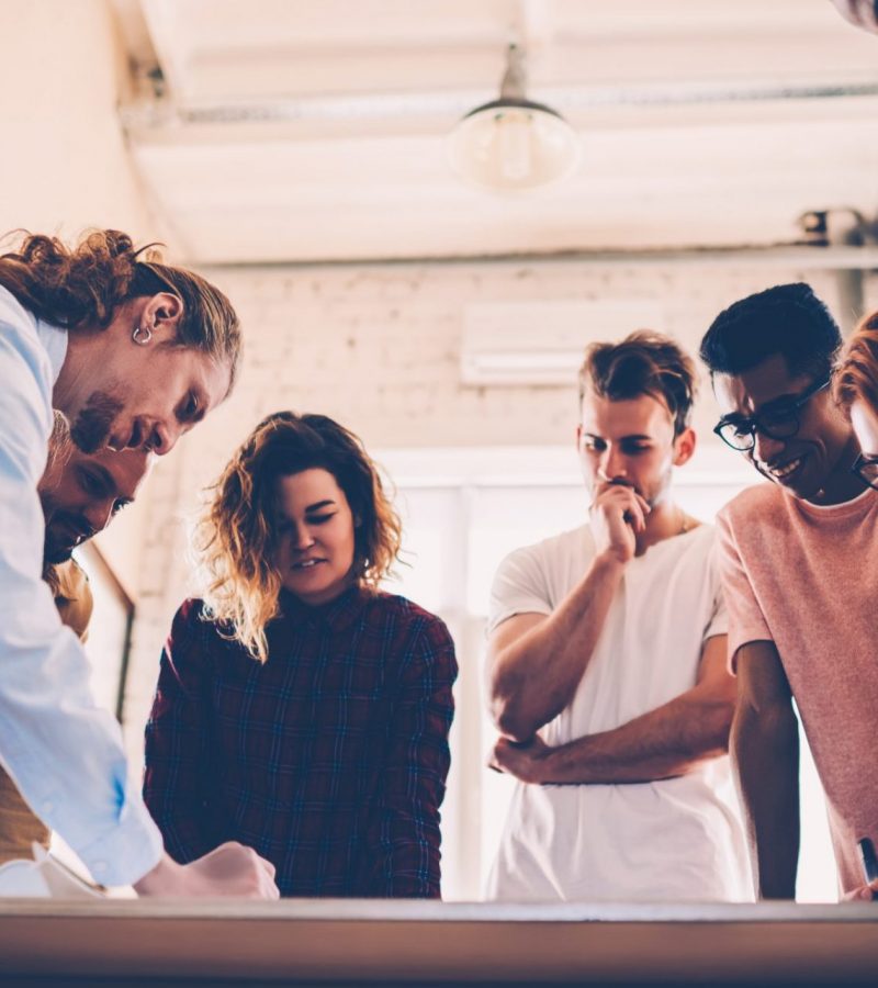 Concentrated group of architects drafting together having consultancy meeting in coworking space, skilled team of creative graphic designers making creative solution working on sketch for project